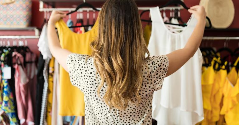 Ung kvinne i klesbutikk En ung kvinne i klesbutikk holder opp en gul og en hvit topp